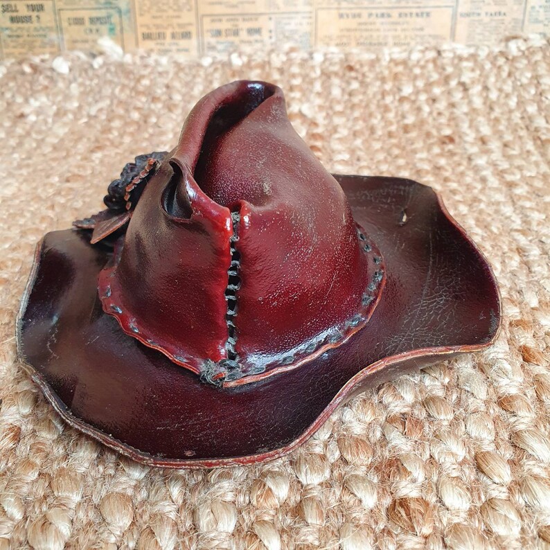 May include: A burgundy leather cowboy hat with a wide brim and a stitched detail around the crown.