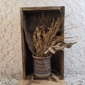 May include: Dried plant material arranged in a rustic wooden box with a brown and black striped ceramic pot. The box has a distressed wood finish.