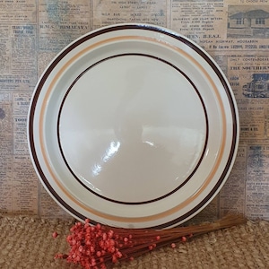 Puede incluir: Un plato de cerámica blanco con un borde marrón y naranja. El plato tiene un acabado brillante y es perfecto para servir una comida.