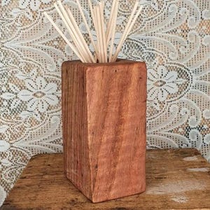 Peut inclure: Un diffuseur d'huiles essentielles rectangulaire en bois avec une finition naturelle. Le diffuseur est rempli de plusieurs roseaux de couleur claire. Le grain du bois est visible. Le diffuseur repose sur une surface en bois.