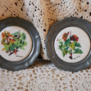 May include: Two vintage pewter coasters with a white ceramic insert featuring a grapevine design. The coasters are labeled "Silvaner" and "Riesling".
