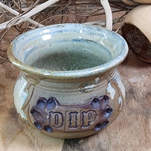 May include: A brown ceramic dip bowl with a light blue glaze. The bowl has a raised, rectangular design with the word "DIP" embossed in the center. The bowl is decorated with paw prints around the edge.