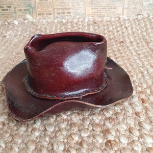 May include: A small, brown leather cowboy hat with a wide brim and a stitched detail around the crown.