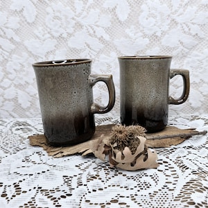 Puede incluir: Dos tazas de cerámica marmoleadas en marrón y blanco con asas. Las tazas tienen un degradado de marrón a blanco.