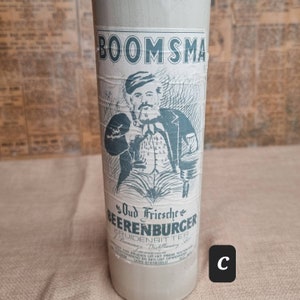 K&ouml;nnte beinhalten: Eine Vintage-Glasflasche mit einem Etikett, auf dem "Oud Friesche Beerenburger Kruidenbitter Bomma's Distilleerderij" steht. Das Etikett zeigt eine Comic-Illustration eines Mannes mit Bart und Pfeife, der ein Glas h&auml;lt. Die Flasche ist mit dem Markennamen "BOOMSMA" gekennzeichnet.