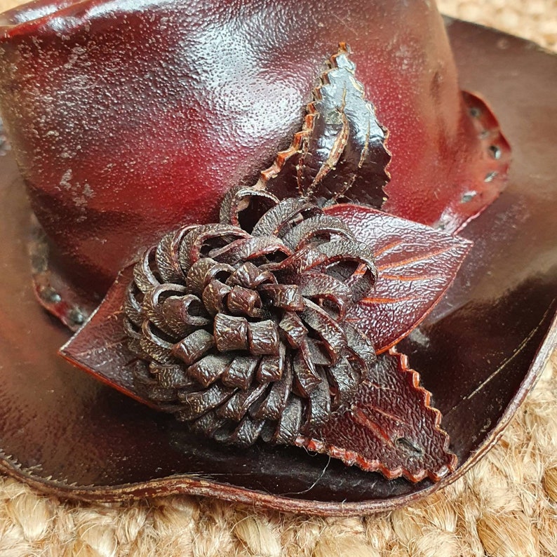 May include: A burgundy leather hat with a brown leather flower design.
