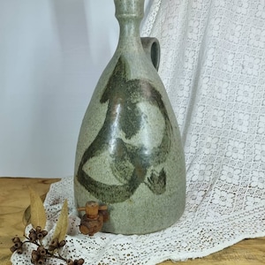 May include: A ceramic jug with a green glaze and black abstract design. The jug has a cork stopper and a wooden spigot.