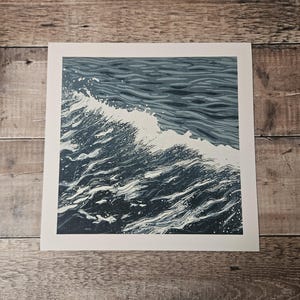 May include: A square print depicting a stylized ocean wave. The artwork features shades of blue and white, with the wave cresting and breaking. The print is set against a white border.