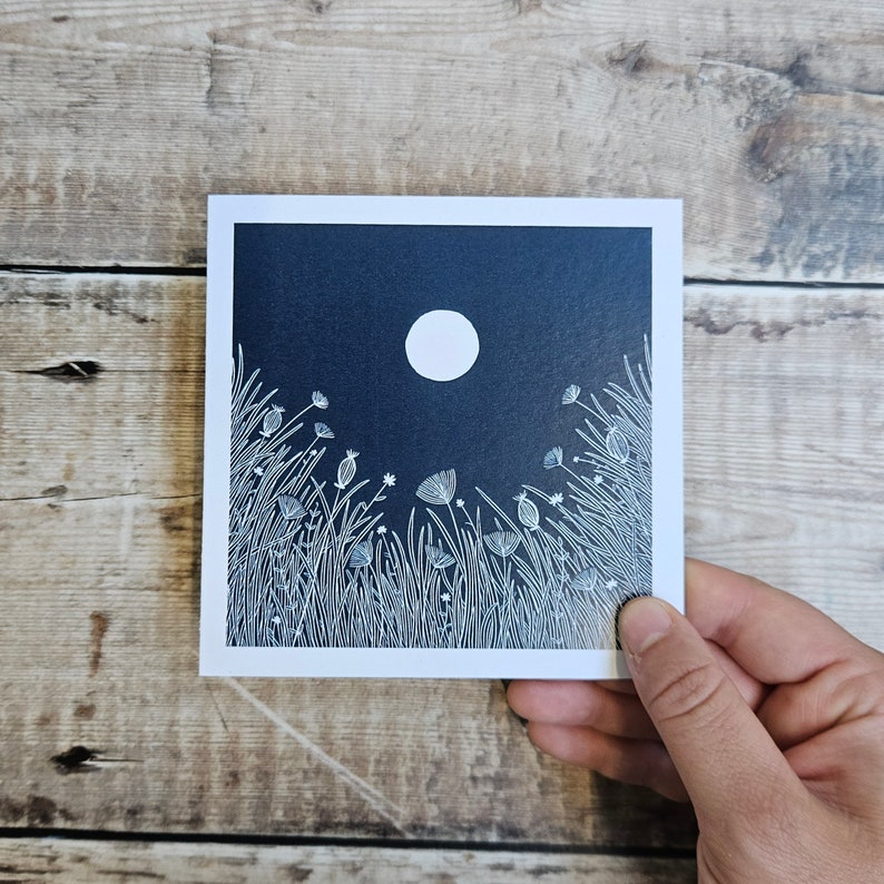 K&ouml;nnte beinhalten: Eine wei&szlig;e Linienzeichnung eines Feldes mit Blumen und Gras unter einem Vollmond vor einem dunkelblauen Hintergrund.