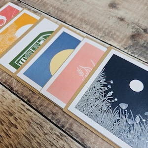 K&ouml;nnte beinhalten: Satz von sechs Gru&szlig;karten mit verschiedenen Illustrationen. Die Karten zeigen eine Vielzahl von Farben und Designs, darunter eine gelbe Sonne, ein gr&uuml;nes Haus, ein blauer Himmel und ein rosa Feld. Die Karten sind alle innen leer, was sie perfekt f&uuml;r jeden Anlass macht.