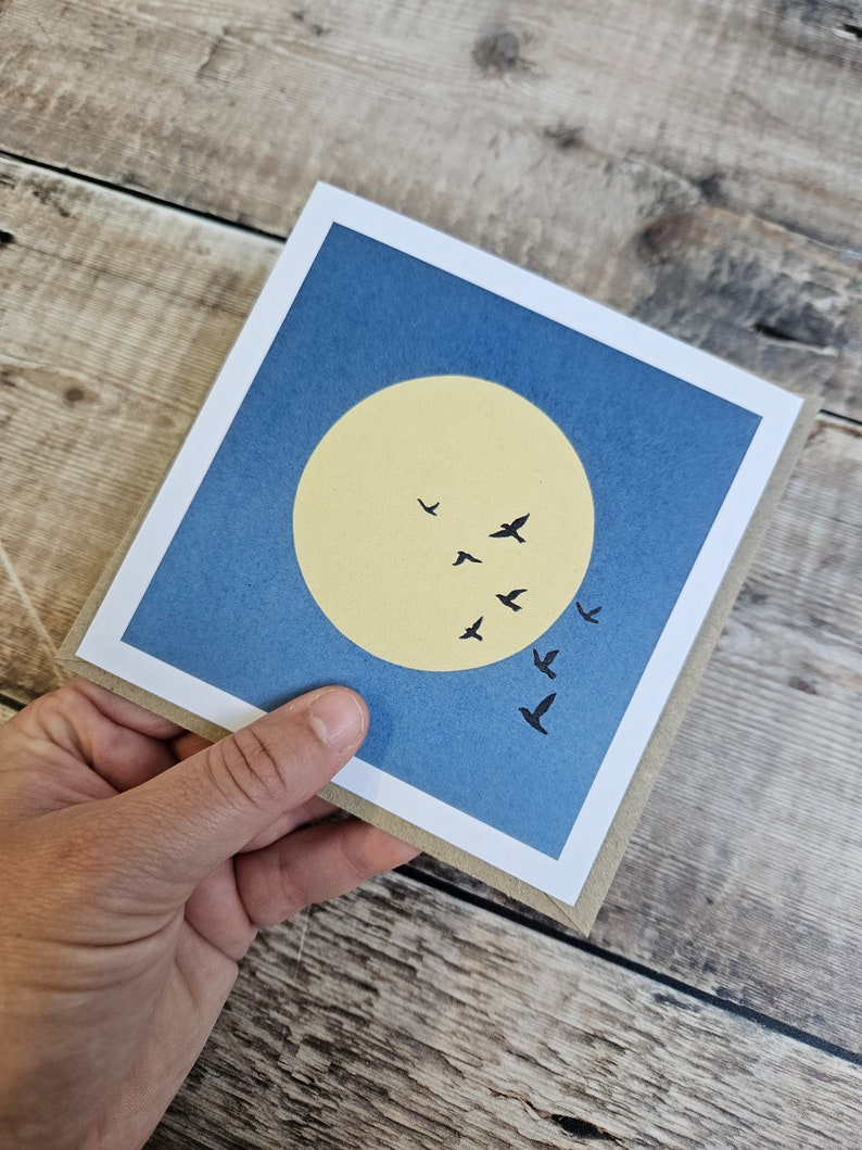 K&ouml;nnte beinhalten: Eine blaue Karte mit einem gelben Kreis und schwarzen Silhouetten von V&ouml;geln, die in V-Formation fliegen. Die Karte hat einen wei&szlig;en Rand.