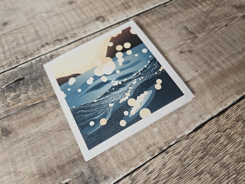 Pu&ograve; includere: Una stampa artistica quadrata raffigurante un paesaggio stilizzato con un corpo d'acqua blu scuro e un cielo colorato. Forme circolari bianche e gialle sono sparse sull'immagine. La stampa ha un bordo bianco.