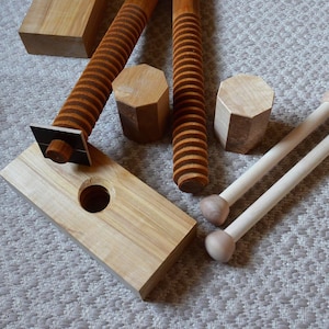 May include: Wooden woodworking clamps and components. The image shows a light-colored wooden base with a round hole, two threaded rods, two dowels with rounded ends, and several wooden blocks. The clamps are made of light-colored wood and have a natural finish.