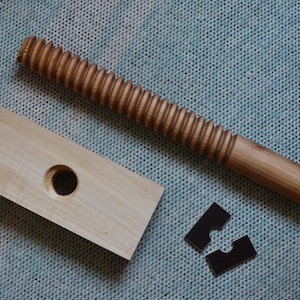May include: A wooden screw clamp with a threaded wooden screw, a wooden base with a hole, and two black metal pieces.