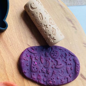 May include: A beige rolling pin with a celestial design of moons, stars, and crystals, alongside a purple clay impression with matching witchy symbols. The rolling pin is approximately 15 cm long, perfect for crafting.