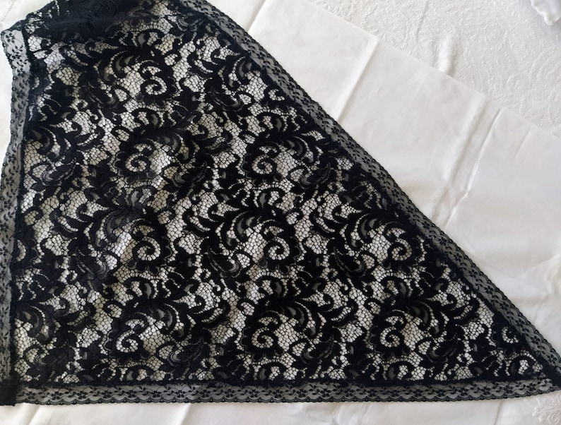 May include: Black lace fabric featuring a floral design. The lace is arranged in a triangular shape, with a detailed border. The fabric is set against a white background, highlighting the intricate design and texture of the lace.
