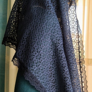 May include: A navy blue lace veil with a scalloped edge. The veil is draped over the head and shoulders, with the intricate floral lace pattern visible. The person is wearing a teal green jumper.