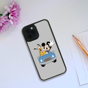Puede incluir: Una funda de teléfono gris con una imagen de dibujos animados de Mickey Mouse y Pluto en un coche azul. Mickey Mouse saluda, y Pluto está sentado. La funda tiene un borde negro.