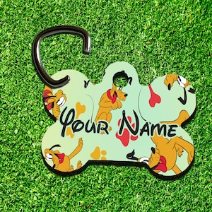 Puede incluir: Una etiqueta para perro de hueso verde con una imagen de dibujos animados de un perro marrón con la lengua roja. La etiqueta tiene un anillo plateado para sujetar a una correa y el texto "Your Name" impreso en ella.