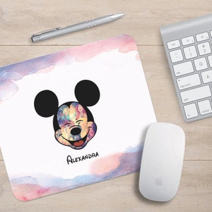 Puede incluir: Una alfombrilla de ratón de acuarela rosa y azul con una cabeza de Mickey Mouse en blanco y negro. La cabeza de Mickey Mouse está hecha de un collage de personajes de Disney. La alfombrilla de ratón está personalizada con el nombre "ALEXANDRA".