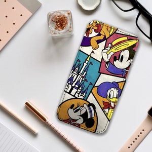 Puede incluir: Una funda de teléfono colorida con los personajes de Disney Mickey Mouse, Minnie Mouse, Donald Duck y Pluto. La funda tiene un diseño de patchwork con un castillo y retratos de personajes. Suministros de oficina rodean la funda.