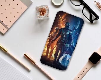 Può includere: Una custodia per telefono nera con un'immagine colorata di personaggi di Star Wars, tra cui un Mandaloriano, un Grogu e un'astronave. Lo sfondo è una nebulosa blu e viola.