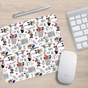 May include: White rectangular mousepad featuring a repeating pattern of Mickey Mouse, landmarks, and phrases such as "Hello", "Ciao", and "Bonjour". A silver pen, a keyboard, and a white mouse are also present.
