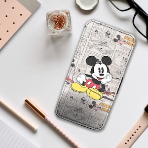 Peut inclure: Un étui de téléphone noir et blanc avec un design de bande dessinée de Mickey Mouse. L'étui présente Mickey Mouse en short rouge, chaussures jaunes et gants blancs. Les mots "Mickey Mouse" sont visibles.