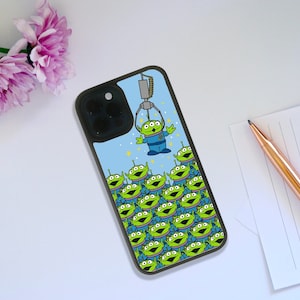 May include: A blue and green phone case featuring a design of multiple green alien characters from the Toy Story franchise. The alien characters are arranged in a pyramid shape with one alien character at the top being lifted by a claw.