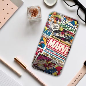 Może przedstawiać: Etui na telefon z kolorowym wzorem komiksowym, przedstawiającym logo MARVEL i ilustracje superbohaterów. Prostokątne etui ma czarną obwódkę. Tekst zawiera "MARVEL Schedule" i "Captain America New York City".