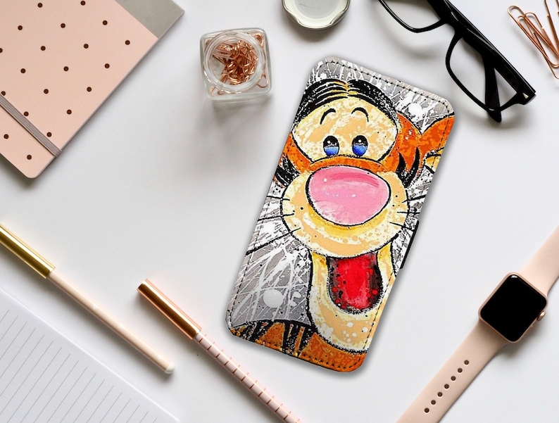 May include: A white phone case with a cartoon illustration of Tigger from Winnie the Pooh. Tigger is orange and black with a red tongue and blue eyes. The background is white with black splatter paint.