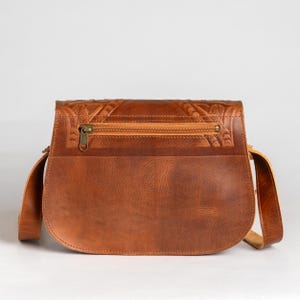 May include: A brown leather crossbody bag with a flap closure and a long adjustable strap. The bag features a zipper pocket and decorative embossed detailing on the flap. The bag is made of a smooth, durable leather.