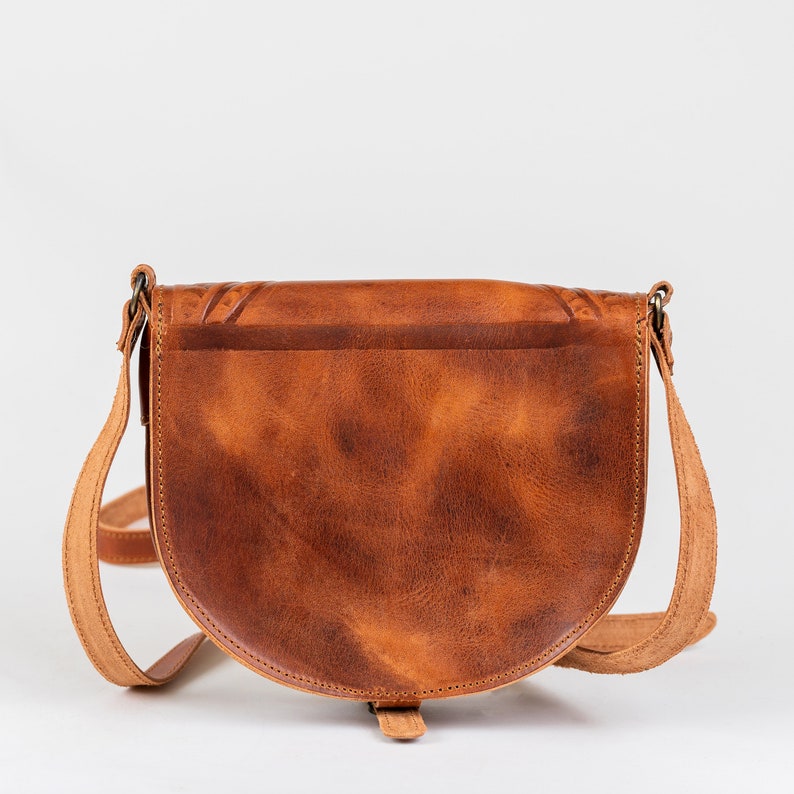 Puede incluir: Un bolso de cuero marr&oacute;n cruzado con cierre de solapa y forma curva. El bolso tiene un aspecto desgastado y un dise&ntilde;o sencillo.
