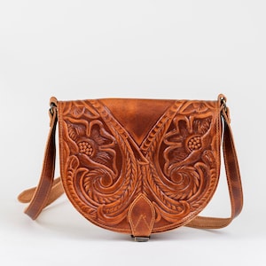 Puede incluir: Un bolso de cuero marr&oacute;n con intrincados detalles florales. El bolso tiene una correa larga y un cierre de solapa.