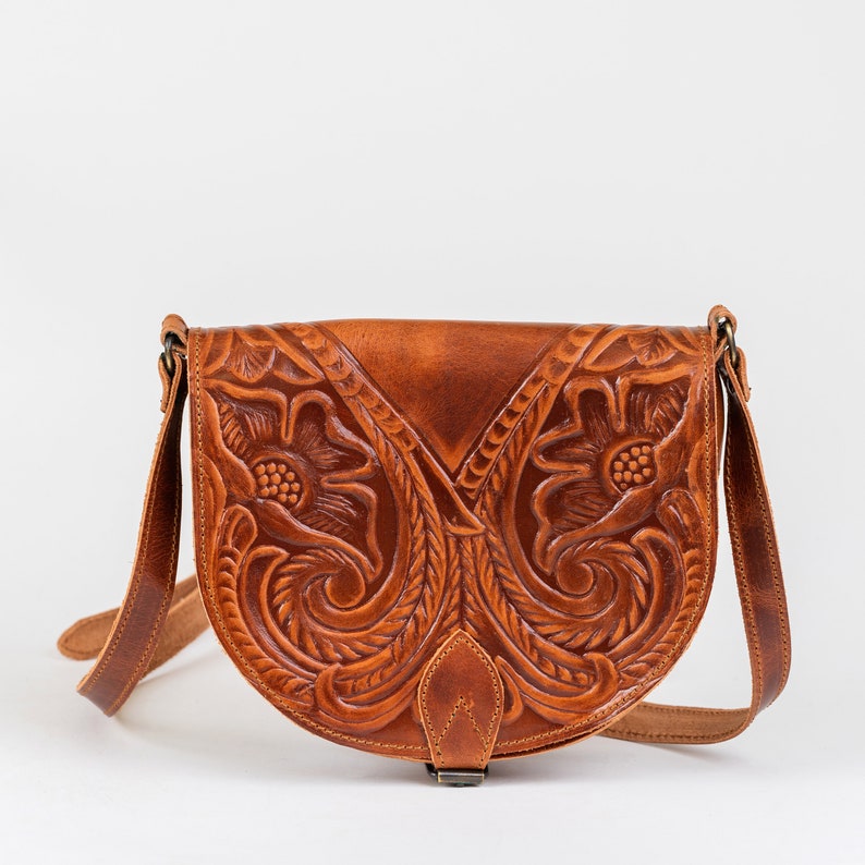 Puede incluir: Un bolso de cuero marr&oacute;n con intrincados detalles florales. El bolso tiene una correa larga y un cierre de solapa.