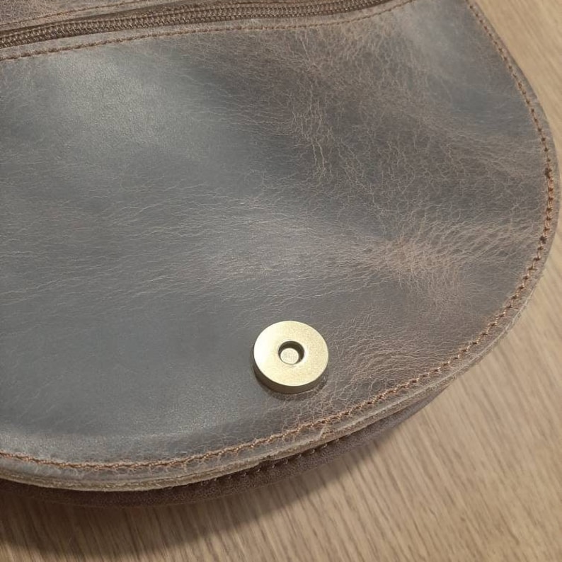 Puede incluir: Primer plano de un bolso de cuero marr&oacute;n con cierre de presi&oacute;n met&aacute;lico dorado.