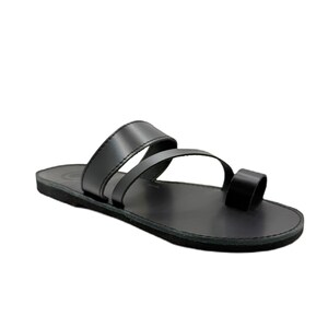 May include: A black flat sandal featuring a smooth footbed and a minimalist design with two wide straps across the midfoot and a separate loop for the big toe. The construction includes a solid black sole and matching black leather-like straps.