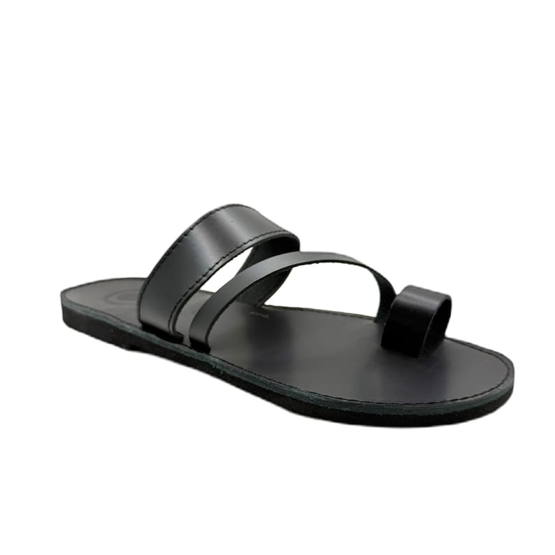 May include: A black flat sandal featuring a smooth footbed and a minimalist design with two wide straps across the midfoot and a separate loop for the big toe. The construction includes a solid black sole and matching black leather-like straps.