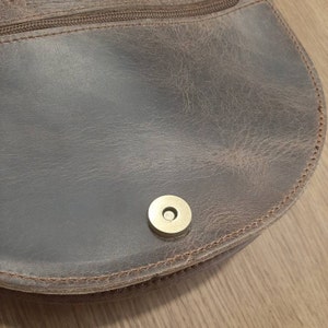 Peut inclure: Un sac en cuir marron avec une fermeture &agrave; glissi&egrave;re et un fermoir magn&eacute;tique en laiton.