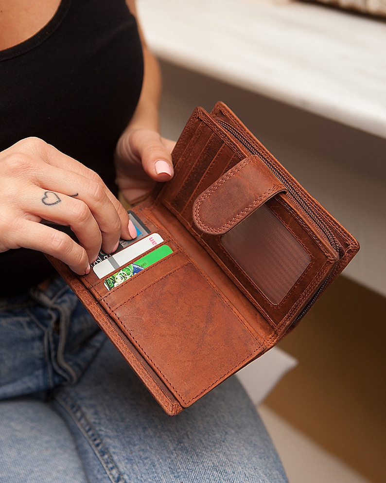 May include: A brown leather wallet with a zip fastening and multiple card slots. The wallet is open and has several cards inside.