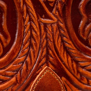 May include: Close-up of a brown leather surface with a detailed embossed floral pattern. The leather has a rich, textured look.