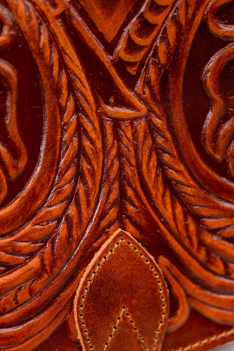 May include: Close-up of a brown leather surface with a detailed embossed floral pattern. The leather has a rich, textured look.