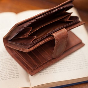 May include: A brown leather wallet with a zip closure. The wallet is open and the interior is visible, showing multiple card slots and a zipped compartment.