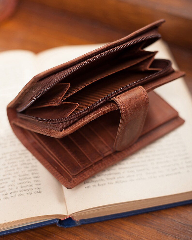 May include: A brown leather wallet with a zip closure. The wallet is open and the interior is visible, showing multiple card slots and a zipped compartment.