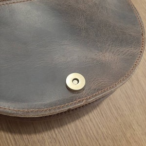 May include: Close-up of a brown leather purse with a brass snap closure.