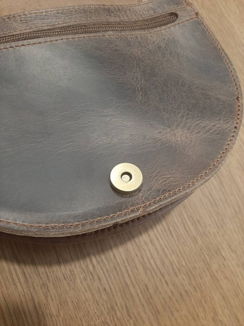 May include: Close-up of a brown leather purse with a brass snap closure.