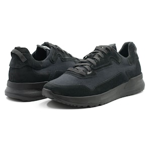 Puede incluir: Un par de zapatillas negras con puntera de ante y parte superior de lona. Las zapatillas tienen una suela blanca y un cord&oacute;n negro.