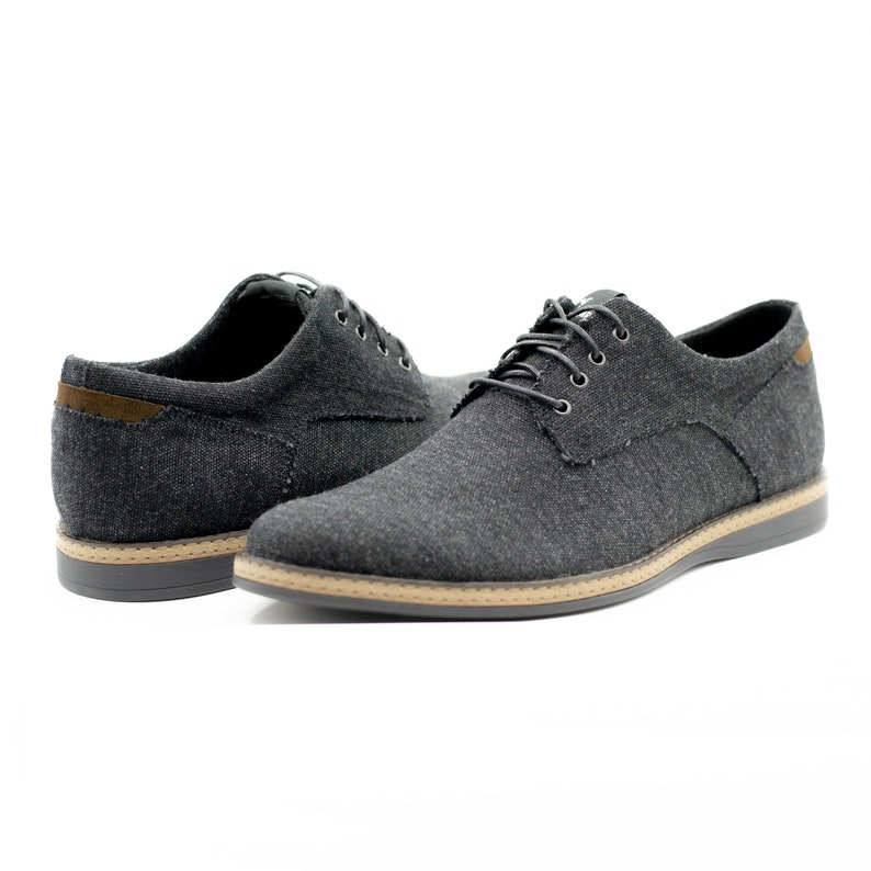 May include: A pair of black canvas lace-up shoes with brown trim around the sole.