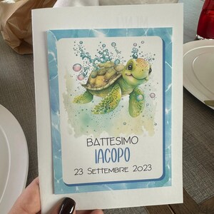 Può includere: Biglietto d'invito per battesimo con illustrazione ad acquerello di una tartaruga marina sorridente e bolle. Il biglietto ha un bordo blu e il testo "Battesimo Iacopo 23 Settembre 2023".