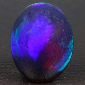 May include: A polished, oval-shaped gemstone with a dark, glossy surface. The stone displays a vibrant play of color, with deep blues, purples, and hints of red and teal. The internal patterns resemble a galaxy.